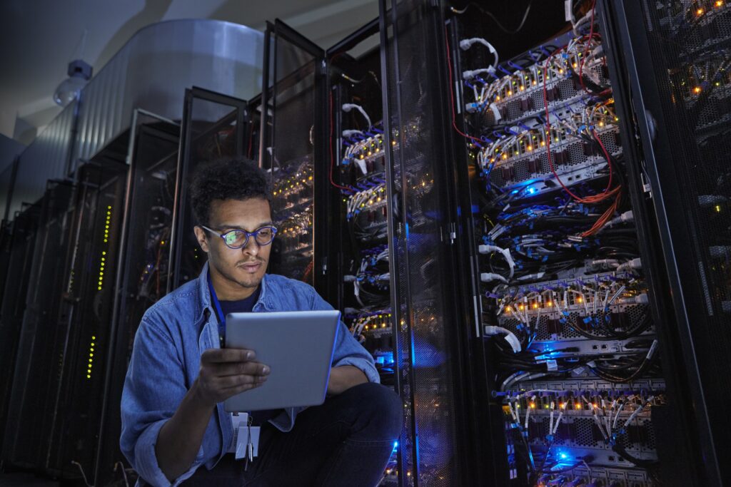 Focused male IT technician using digital tablet in dark server room oneworldlogixcom data center migration